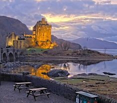 an old castle sits on the edge of a body of water with picnic tables in front of it