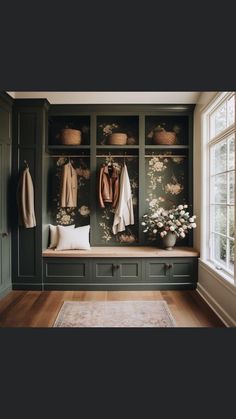 an entryway with green cabinets and floral wallpaper on the walls, two coats hanging from hooks