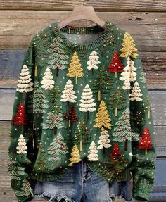 a green sweater with christmas trees on it is hanging from a hanger in front of a wooden wall