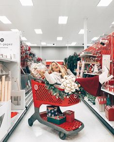 a woman sitting in a red shopping cart with christmas decorations on the shelf behind her