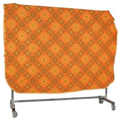 an orange and yellow quilt on a metal rack with wheels for carrying the blanket or bedding