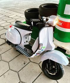 a white scooter is parked next to some tires on the ground near a green barrel