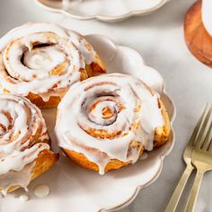 three cinnamon rolls sitting on top of a white plate next to a fork and knife