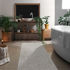 a bath tub sitting next to a white sink in a bathroom under a window with potted plants