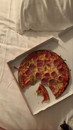 a pepperoni pizza in a box with one slice missing from it on a bed