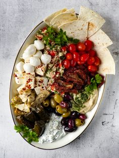 a plate filled with different types of food on top of a white tablecloth next to tortillas and olives