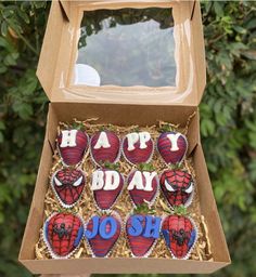 a box filled with decorated cookies in the shape of spiderman's faces and words