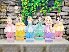 four paper dolls sitting on top of a table next to a stone wall and green leaves