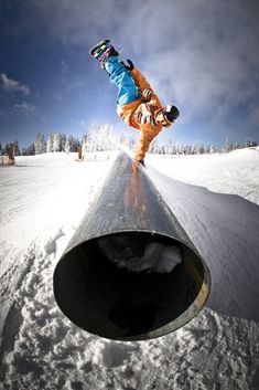 a man riding a snowboard down the side of a pipe on top of snow covered ground