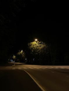 an empty street at night with the lights on and trees in the dark behind it