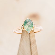 a ring with a large green stone on it's side sitting on top of a wooden stand