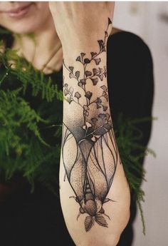 a woman is holding her arm up with flowers and leaves tattooed on it's wrist