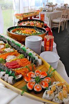 an assortment of sushi and other food items on a long table with white linens