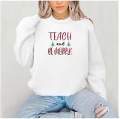 a woman wearing a white sweatshirt with the words teach and be merry on her chest