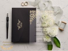 wedding stationery with white flowers and greenery next to it on a marble surface