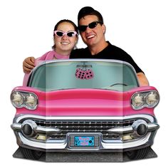 two people are posing in the front of a pink car with hearts on its hood