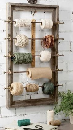 a wooden frame with yarn and scissors hanging on it's side, in front of a white brick wall