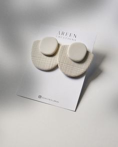 a pair of white earrings sitting on top of a piece of paper next to a card