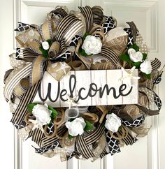 a welcome wreath hanging on the front door with ribbon and flowers around it that reads, welcome