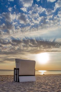 a chair sitting on top of a sandy beach next to the ocean under a cloudy sky