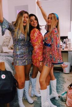 three beautiful young women standing next to each other in front of a bed wearing boots