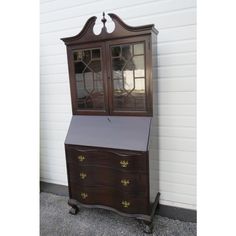 an old wooden desk with glass doors on it's top and bottom drawers in front of a white wall