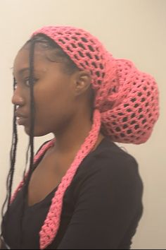 a woman wearing a pink crochet hat with braids on her head and looking off to the side