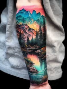 a man's arm with a colorful mountain scene and lake tattoo on the forearm