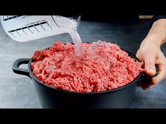 a person pouring water into a pot filled with ground beef