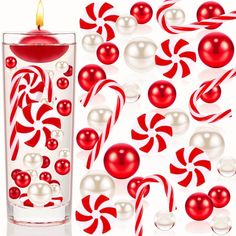 a red candle sitting inside of a tall glass filled with candy canes and balls