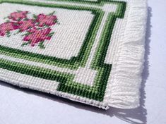 a cross - stitch square with pink flowers on green and white squares, sitting on a table