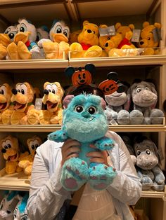 a person holding a stuffed animal in front of shelves full of stuffed animals and mickey mouse heads