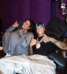 two people sitting on a couch in a room with purple walls and black leather furniture