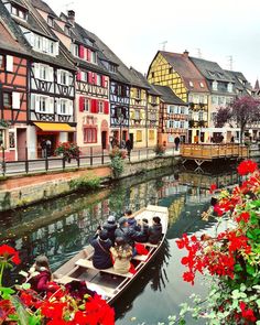 several people are in a boat on the water near some buildings and flowered bushes