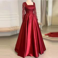 Step into timeless elegance with our exquisite Red Satin Evening Gown. Designed with a sophisticated square neckline and adorned with intricate beadwork, this gown is the epitome of chic. The long sleeves feature sheer, beaded detailing that adds an ethereal touch, making it perfect for formal events, galas, or upscale parties.Crafted from premium quality satin, this dress offers a luxurious gleam and a comfortable fit, allowing you to move with grace and confidence. The full-length, A-line silhouette flatters all body types, while the cinched waist accentuates your natural curves, creating a stunning hourglass figure. The fabrics rich, deep red hue is both bold and timeless, ensuring you stand out in any crowd.Pair this glamorous gown with your favorite accessories and heels for a complet Red Satin Maxi Dress, Gaun Design, Red Long Gown, Gown Dress Party Wear, Wedding Frocks, Party Wear Gowns, Long Gown Design, Satin Evening Gown, Evening Gowns With Sleeves