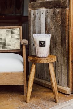 a candle sitting on top of a wooden stool next to a chair with a white pillow