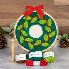 a green wreath with red ribbon and two balls of yarn in front of it on a table