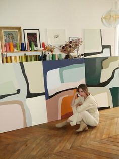 a woman kneeling on the floor in front of a painting and holding her hand up to her face