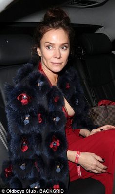 a woman sitting in the back seat of a car wearing a black and red fur coat