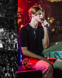 a young man sitting on top of a bench holding a microphone in front of a crowd