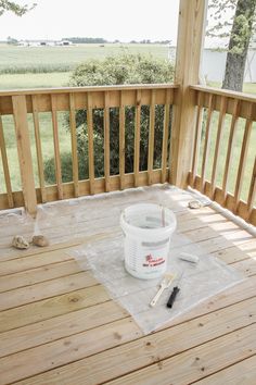 a bucket sitting on top of a wooden deck next to a paint roller and brush