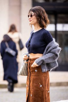 a woman in a skirt and sweater is walking down the street with her hand on her hip