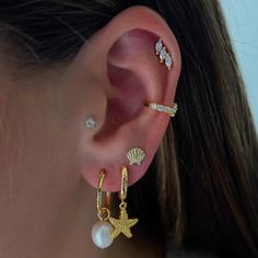 a close up of a person wearing ear piercings with pearls and seashells on them