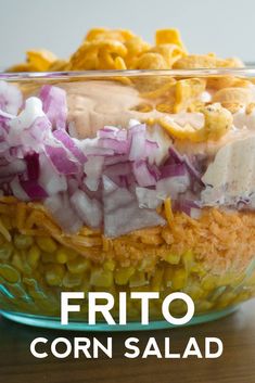 a glass bowl filled with corn, onions and other foods on top of a wooden table