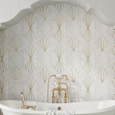 a white bath tub sitting next to a wall with gold art deco designs on it