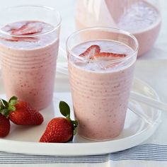 two glasses filled with smoothie and strawberries on a plate