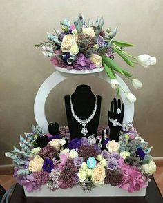 an elaborate display with flowers and jewelry on top of a white stand in front of a wall