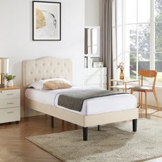 a white bed sitting next to a window on top of a wooden floor in a bedroom