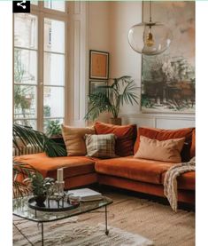 a living room with orange couches and plants on the wall, rugs in front of large windows