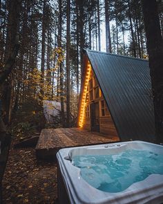 a hot tub sitting next to a wooden cabin in the woods with lights on it